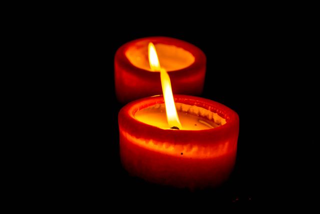 This image shows a close-up of two lit red candles emitting warm and serene light in dark surroundings. It can be used for themes related to romance, meditation, tranquility, spa settings, or creating a soothing mood. It is also ideal for greeting cards, home decor blogs, and articles about candlelit ambiance.