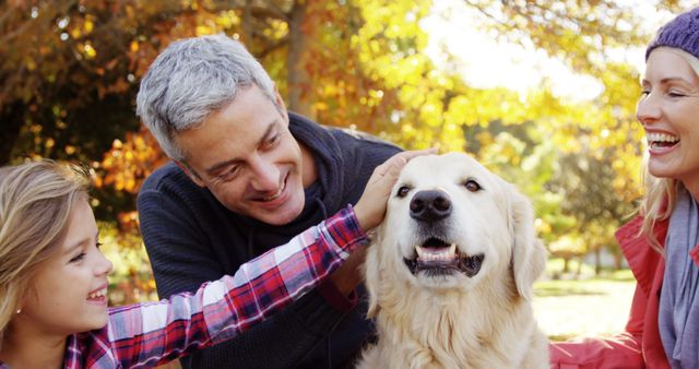 A middle-aged Caucasian man and woman enjoy a sunny day at the park with a young girl, all smiling as they pet a golden retriever, with copy space. Their joyful interaction with the dog highlights the happiness pets bring to family moments.