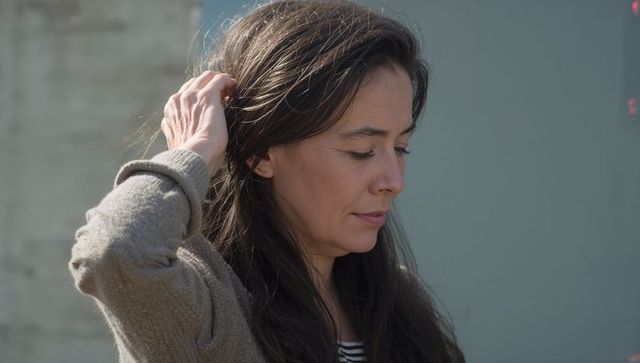 Serene side profile woman touching long dark hair near urban wall in beige sweater