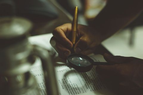 Person examining documents with magnifying glass