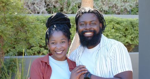 African couple smiling and embracing in sunlit courtyard holding smartwatch, warm lifestyle portrait