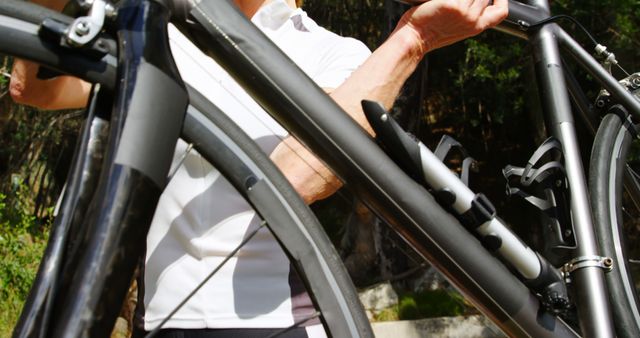 Close-up view of a cyclist holding a black bicycle, showcasing detailed parts of the bike. The cyclist is outdoors, promoting an active and healthy lifestyle. Ideal for use in content related to cycling, fitness, outdoor activities, sports gear, and health-conscious living.