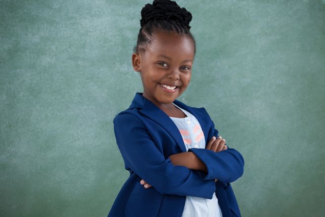 This image depicts a young girl in business attire standing with her arms crossed and smiling confidently. Ideal for use in educational materials, advertisements promoting youth empowerment, leadership programs, or articles about future leaders and professional development in children.