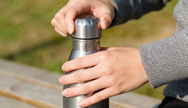 Hands twisting cap off stainless steel thermos on park bench — outdoor hydration moment