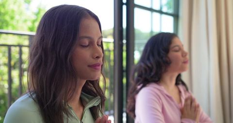 Mother and daughter practicing mindfulness together on sunlit balcony during morning prayer