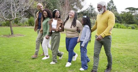 Multigenerational Black Family Walking and Laughing in Park Wearing Sweaters and Jeans
