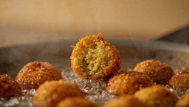 Crispy golden falafel ball sizzling in bubbling oil, split open revealing vibrant green herb center