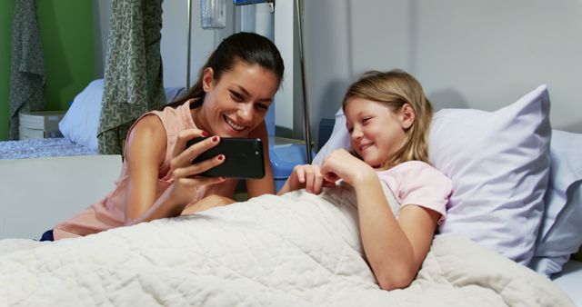 Mother and daughter smiling at phone in hospital bed - Download Free Stock Images Pikwizard.com