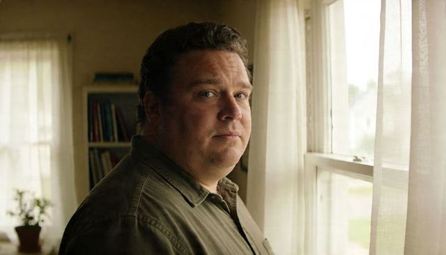 Introspective man looking out sunlit window in warm home interior with sheer curtains