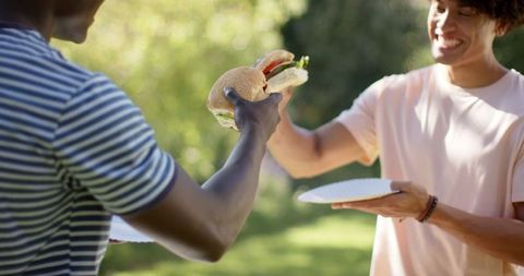 Friends Sharing Hamburger in Sunlit Park Gathering
