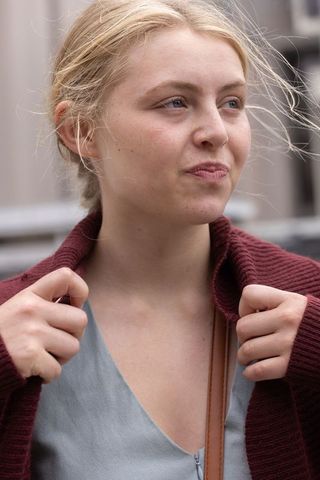 Young woman adjusting maroon cardigan while gazing away urban natural light portrait
