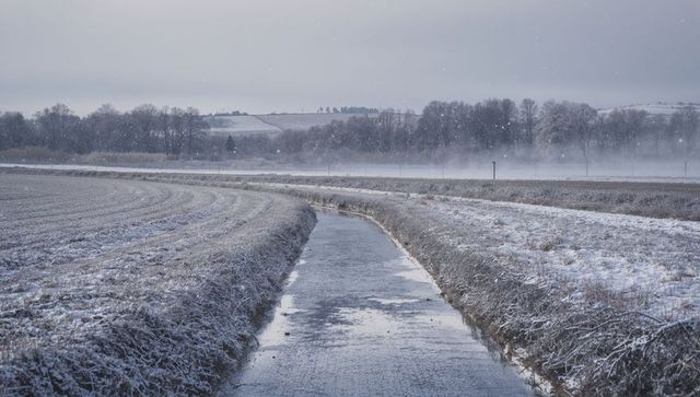Winding icy lane through frosty rural fields with misty winter horizon
