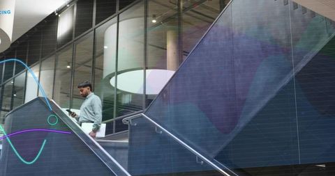 Businessman walking up atrium stairs holding phone and folder in modern glass lobby