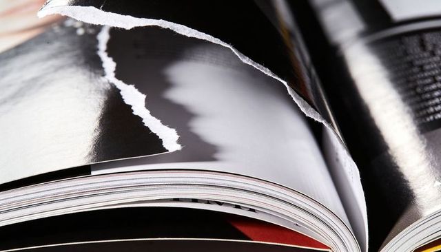 Torn glossy magazine page curling macro close-up showing paper texture and edge highlights