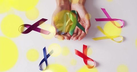 Hands holding colorful awareness ribbons with yellow bokeh