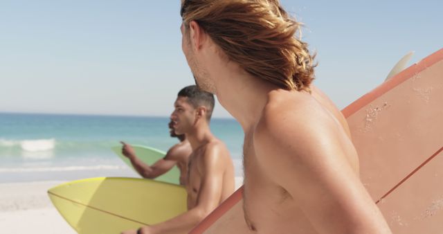 Three young men carrying surfboards on a sunny beach, looking towards the ocean. Ideal for promoting coastal tourism, surfing gear, outdoor activities, beachwear, or advertisements focusing on an active lifestyle and camaraderie.