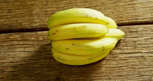 A bunch of ripe bananas rests on a wooden surface, offering a natural and healthy snack option. Bananas are a popular fruit known for their potassium content and ease of eating on the go.