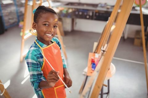 Creative young girl painting on easel in art classroom