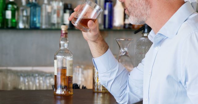 Man enjoying a glass of whiskey at a bar counter in a casual setting. Ideal for marketing alcoholic beverages, promoting bars, nightlife and leisure activities.