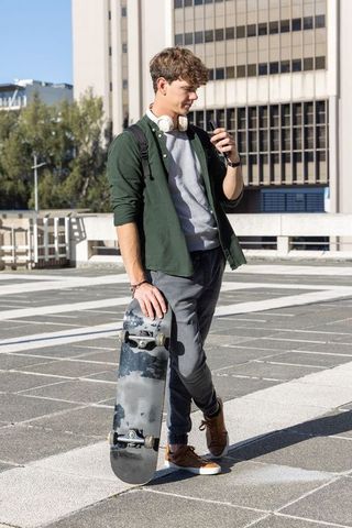 Skateboarder standing on rooftop deck holding board while checking smartphone