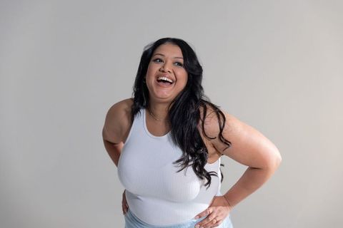 Mid-adult woman laughing and leaning forward hands on hips wearing white tank top