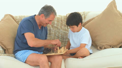 Grandfather and Grandson Enjoying a Chess Match on Sofa
