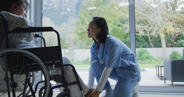 Asian female doctor talking to female patient in wheelchair and arranging her feet at hospital. medicine, health and healthcare services.