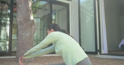 African american woman stretching on gravel patio near glass doors during morning workout