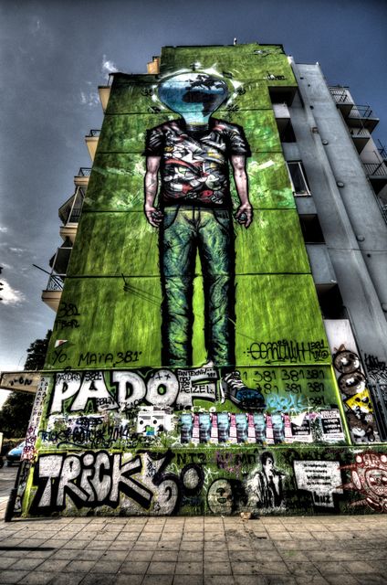Large mural painted on side of urban building shows astronaut with fishbowl for a head, surrounded by graffiti and street art, evokes sense of creativity and urban culture, perfect for showcasing contemporary art, street culture aesthetics, or urban themed projects.