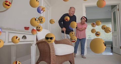 Caregiver guiding mature asian couple walking with cane at home amid floating joyful emoji