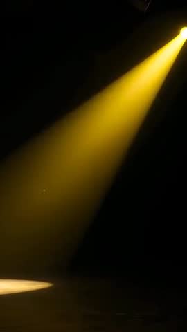 Vertical video casting yellow spotlight beam and pool on dark stage with theatrical haze