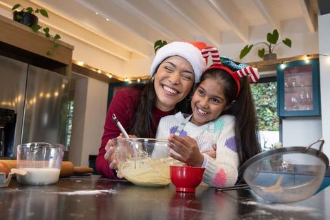 Indian mother and daughter baking together wearing santa hats in cozy modern kitchen