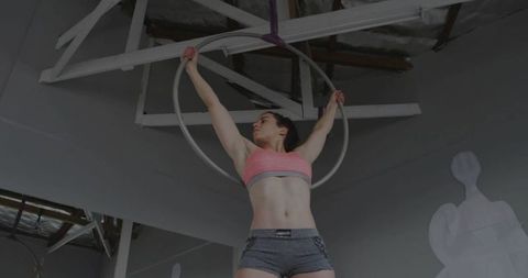 Confident aerialist performing aerial hoop acrobatics in minimalist studio