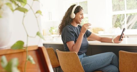 African american woman enjoying virtual call at sunny kitchen counter with headphones