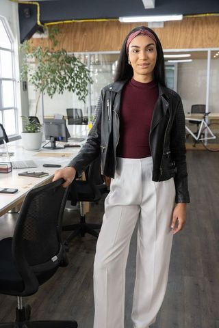 Confident professional woman standing in modern coworking office wearing leather jacket