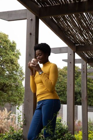 Woman standing under pergola holding mug in peaceful garden
