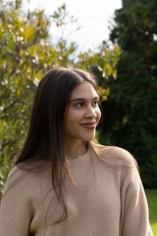 Smiling young woman looking away in garden wearing beige knit sweater, serene outdoor portrait