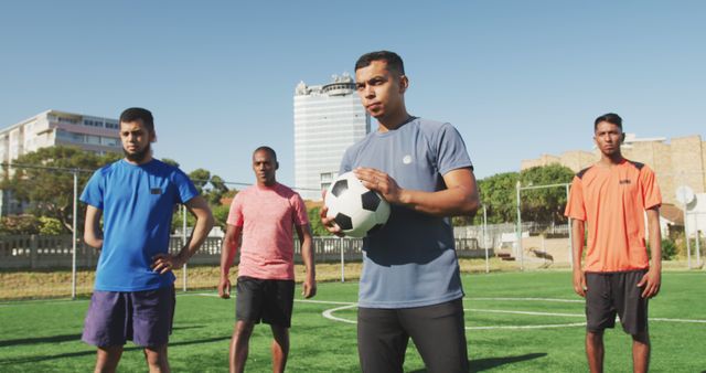 Diverse male football players training and holding ball on outdoor pitch - Download Free Stock Photos Pikwizard.com