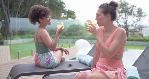 Women relaxing poolside sipping citrus cocktails on loungers, casual summer moments