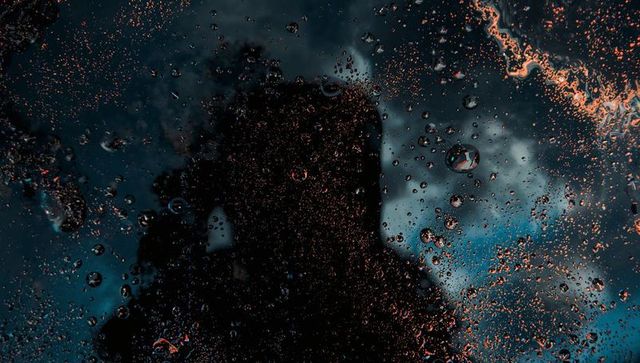 Moody urban silhouette reflected on rain-speckled glass with cinematic blue and orange highlights