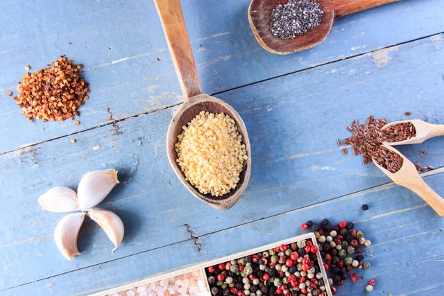 Colorful display of various spices and a garlic clove arranged on a rustic blue wooden table. Ideal for use in culinary blogs, recipe websites, and healthy eating advertisements.