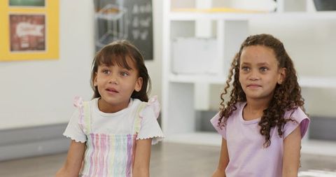 Two girls sitting in bright classroom listening and learning together