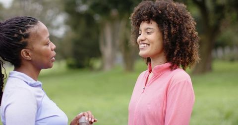 Diverse women chatting after exercising in park while holding water bottle