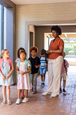 African american teacher leading elementary students down sunlit school corridor