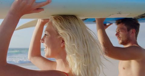 Young couple carrying surfboard at beach