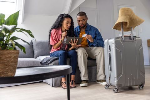 Diverse couple planning trip using tablet and boarding pass beside suitcase in modern loft