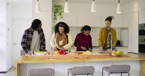 Diverse friends wearing casual clothes chopping fruit and preparing salad on bright kitchen island
