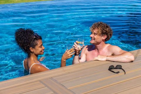 Couple clinking citrus drinks while relaxing in backyard pool on sunny day