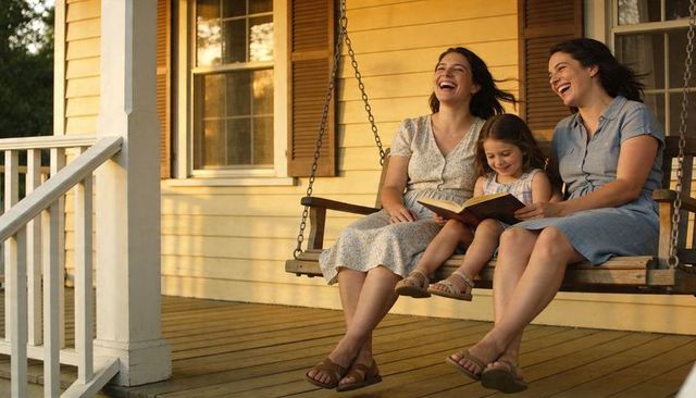 Sunlit porch swing laughing family reading together on warm summer evening