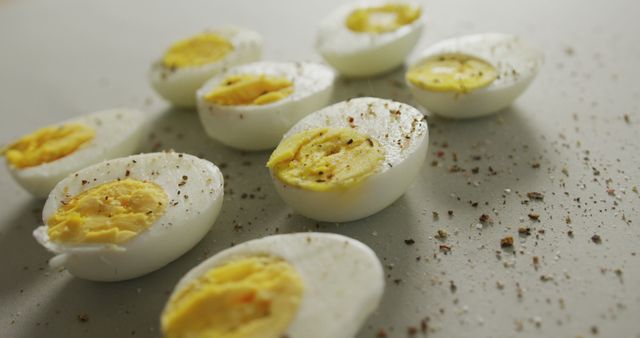 This image showcases sliced boiled eggs sprinkled with black pepper on a white surface. Ideal for illustrating topics related to healthy eating, protein-rich diets, breakfast ideas, snacks, or nutritional information. Suitable for use in food blogs, diet plans, social media posts, or culinary websites.